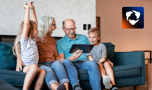 An older couple sitting on the couch with two small grandchildren, watching a livestream on a tablet